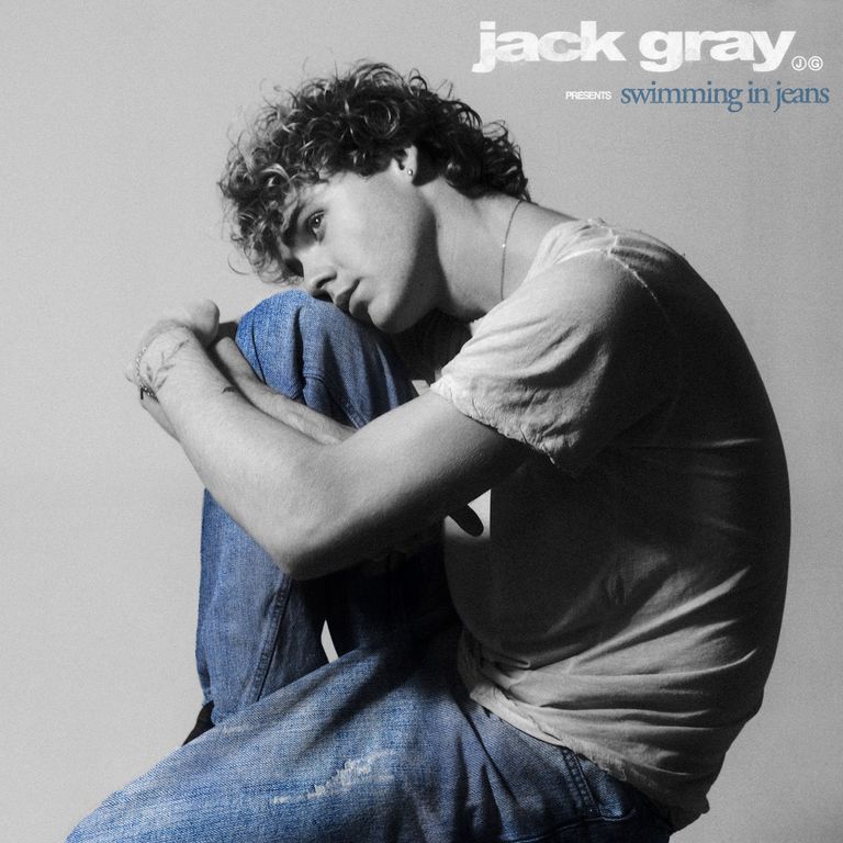 Album artwork for Jack Gray Presents Swimming in Jeans, showing the curly-haired artist curled up in blue denim jeans against a grey background.